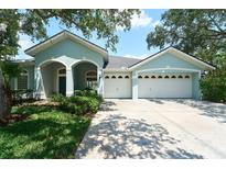 Charming home with a three-car garage and covered entryway, surrounded by lush landscaping and mature trees at 10219 Millport Dr, Tampa, FL 33626