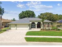 Charming single-story home with a three-car garage, manicured lawn, and inviting brick-paved driveway at 1521 Brittany Ct, New Port Richey, FL 34655