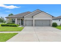 Beautiful single-story home with a manicured lawn, gray facade, and three-car garage at 6670 Paden Wheel St, Zephyrhills, FL 33541