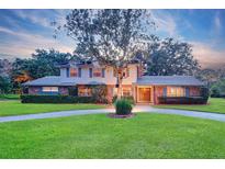 Charming two-story home featuring brick accents, a well-manicured lawn, mature landscaping, and a circular driveway at 1670 Fox Rd, Clearwater, FL 33764
