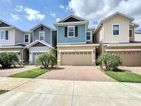 View of charming two-story townhomes with colorful facades, well-manicured lawns, and brick driveways on a sunny day at 34187 Rogallo Ln, Wesley Chapel, FL 33545