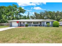 Charming single-story home with lush lawn, mature trees, and a driveway leading to an attached garage at 5068 Lakewood Dr, Ridge Manor, FL 33523