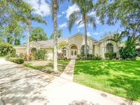 Charming single-story home featuring a manicured lawn, elegant arched windows, and lush tropical landscaping at 3910 Saywood Ct, Palm Harbor, FL 34685