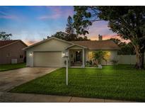 Charming single-story home featuring a well-manicured lawn, a driveway, and appealing curb appeal at dusk at 1562 Coastal Pl, Dunedin, FL 34698