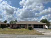 Charming single-story home with a well-manicured lawn, mature trees, and a screened front porch at 8130 Shalom Dr, Spring Hill, FL 34606