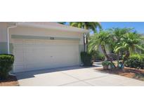 Attached two-car garage featuring a concrete driveway, manicured shrubbery, and tropical palm trees on a sunny day at 834 Tremont Greens Ln # 137, Sun City Center, FL 33573
