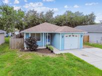 Charming single-story home featuring light blue siding, a well-manicured lawn, and an attached one-car garage at 105 1St Se Ave, Lutz, FL 33549