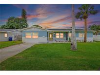 Charming blue single-story home featuring a well-manicured lawn and complemented by two palm trees at sunset at 4230 Indianapolis Ne St, St Petersburg, FL 33703