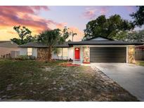 Charming single-story home with stone accents, a red door, fresh landscaping, and a dark garage door at 622 Cedar Grove Dr, Brandon, FL 33511