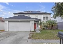 Two-story home featuring an attached two-car garage, solar panels, and a red front door at 10337 River Bream Dr, Riverview, FL 33569