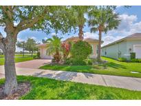 Well-maintained home with tropical landscaping, mature trees, and a brick driveway at 16227 Cape Coral Dr, Wimauma, FL 33598