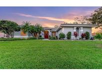 Charming home featuring lush green lawn, mature trees, and a red front door, under a lovely pastel sunset sky at 137 Woodcreek E Dr, Safety Harbor, FL 34695