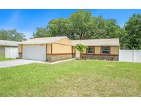 Charming single-story home with a large front yard, light-yellow paint, stone accents, and an attached two-car garage at 3072 Sugar Bear Trl, Palm Harbor, FL 34684