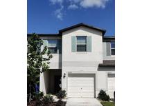 Two-story townhouse showcases a white exterior, complemented by vibrant landscaping under a clear blue sky at 4505 Globe Thistle Dr, Tampa, FL 33619