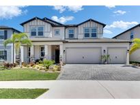 Beautiful two-story home boasts lush landscaping, a three-car garage, and a light gray brick paver driveway at 5026 Bromeliad Ave, Wimauma, FL 33598
