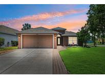 Charming single-story home featuring a well-manicured lawn, two car garage, and a beautiful sunset sky at 2708 Dolphin Watch Ct, Holiday, FL 34691