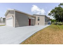A charming home featuring tan siding, a garage, and a red front door with a freshly painted driveway at 8471 Fantasia Park Way, Riverview, FL 33578