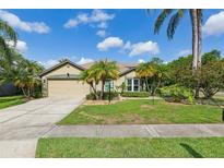 Charming single-story home featuring a manicured lawn, mature palm trees, and a two-car garage at 892 Crestridge Cir, Tarpon Springs, FL 34688
