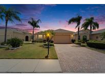 Charming single-story home featuring a brick driveway, lush landscaping, and beautiful palm trees at sunset at 1643 Emerald Dunes Dr, Sun City Center, FL 33573