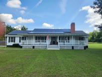 Inviting home with a charming front porch, solar panels, a brick chimney and a lush green lawn at 17430 Spring Valley Rd, Dade City, FL 33523