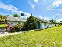 Quaint single-story home featuring a blue door, lush landscaping, and a well-maintained front lawn under a bright, sunny sky at 14318 Guava St, Hudson, FL 34667