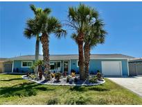Charming home featuring light-blue siding, a well-manicured lawn, and beautiful landscaping with palm trees at 12300 4Th E St, Treasure Island, FL 33706