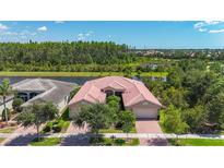 Charming single-story home features a red-tiled roof and lush landscaping, nestled next to a serene lake at 15860 Aurora Lake Cir, Wimauma, FL 33598