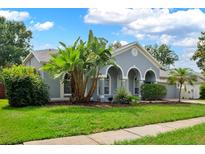 Charming single-story home featuring arched entrance, blue paint, lush landscaping, and a well-manicured lawn at 3703 Treeline Dr, Valrico, FL 33596