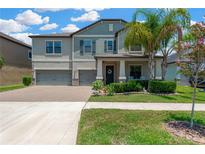 Charming two-story home featuring a brick driveway, manicured lawn, and inviting front porch with palm trees at 11612 Sunburst Marble Rd, Riverview, FL 33579