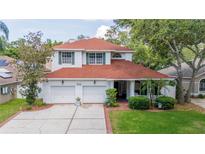 Charming two-story home boasts a red roof, a two-car garage, and a well-manicured lawn surrounded by mature trees at 2015 Long Branch Ln, Clearwater, FL 33760