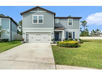 Charming two-story home with light blue siding, a well-manicured lawn, and an attached two-car garage at 30572 Thunderbird Dr, Wesley Chapel, FL 33545