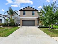 Charming two-story home with a gray garage door, a well-manicured lawn, and landscaped garden beds at 9605 Channing Hill Dr, Sun City Center, FL 33573
