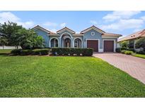 Charming blue home features a well-manicured lawn, lush landscaping, and a brick driveway leading to a two-car garage at 10645 Ruffino Ct, Trinity, FL 34655