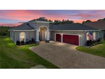 Beautiful single Gathering home with a brick driveway, three car garage and manicured lawn under a colorful sunset sky at 34652 Heavenly Ln, Dade City, FL 33525