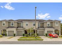 Tan townhomes with garages and a red car parked in front under a sunny blue sky at 6924 Towne Lake Rd, Riverview, FL 33578