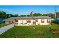 Charming single-story home boasts a well-manicured lawn, covered carport, and a welcoming porch with blue seating at 5409 Antigua Dr, Zephyrhills, FL 33541