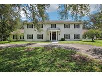 A charming two-story white home boasts mature trees, black shutters, and a circular driveway at 12433 Kelso Rd, Thonotosassa, FL 33592