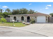 Charming stone-clad home featuring a well-manicured lawn, flower beds and an attached one car garage at 8918 Carmen Ln, Port Richey, FL 34668