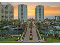 Stunning aerial view of beachfront condo complex with lush landscaping, tennis courts, and ocean views at sunset at 1180 Gulf Blvd # 402, Clearwater Beach, FL 33767