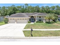 Charming home featuring a three-car garage, tile roof, lush lawn, and meticulously manicured landscaping at 4049 Wellington Pkwy, Palm Harbor, FL 34685