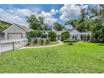 Charming single-story home features a white picket fence, lush lawn, and a cozy pergola-covered patio, perfect for outdoor living at 118 S Manhattan Ave, Tampa, FL 33609