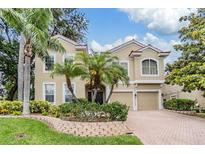 Two-story tan house featuring an attached two car garage and lush landscaping with palm trees at 2354 Messenger Cir, Safety Harbor, FL 34695