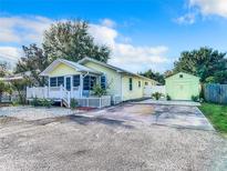 Charming yellow home with a picket fence, covered porch, and a matching storage shed, set against a bright blue sky at 2928 W Arch St, Tampa, FL 33607