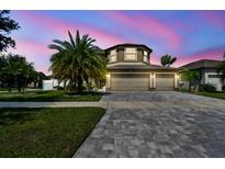 Charming exterior with paver driveway, three-car garage and well-maintained landscaping at dusk at 11602 Sunburst Marble Rd, Riverview, FL 33579