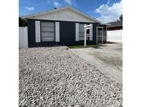 View of single-story home with dark siding, white trim, stone ground cover, and 'For Sale' sign at 9106 Telford Ct, Tampa, FL 33615
