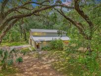 Secluded two-story home with a metal roof nestled among mature trees and a lush landscape at 7189 Griffin Rd, Brooksville, FL 34601
