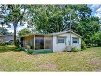 Exterior view of a house with a screened porch and green trim, surrounded by lush trees at 38839 Miller Ave, Zephyrhills, FL 33542