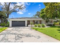 Charming single-story home with a well-manicured lawn, gray garage door, and beautiful landscaping at 125 Live Oak Ln, Largo, FL 33770