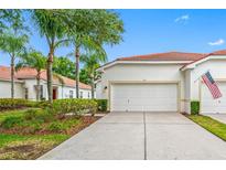 Charming home featuring a white exterior, red tile roof, palm trees, and a two-car garage at 10255 Devonshire Lake Dr, Tampa, FL 33647