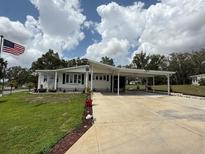 Charming single-story home featuring a long driveway, carport, and manicured lawn under a partly cloudy sky at 12021 Club House Rd, Brooksville, FL 34613